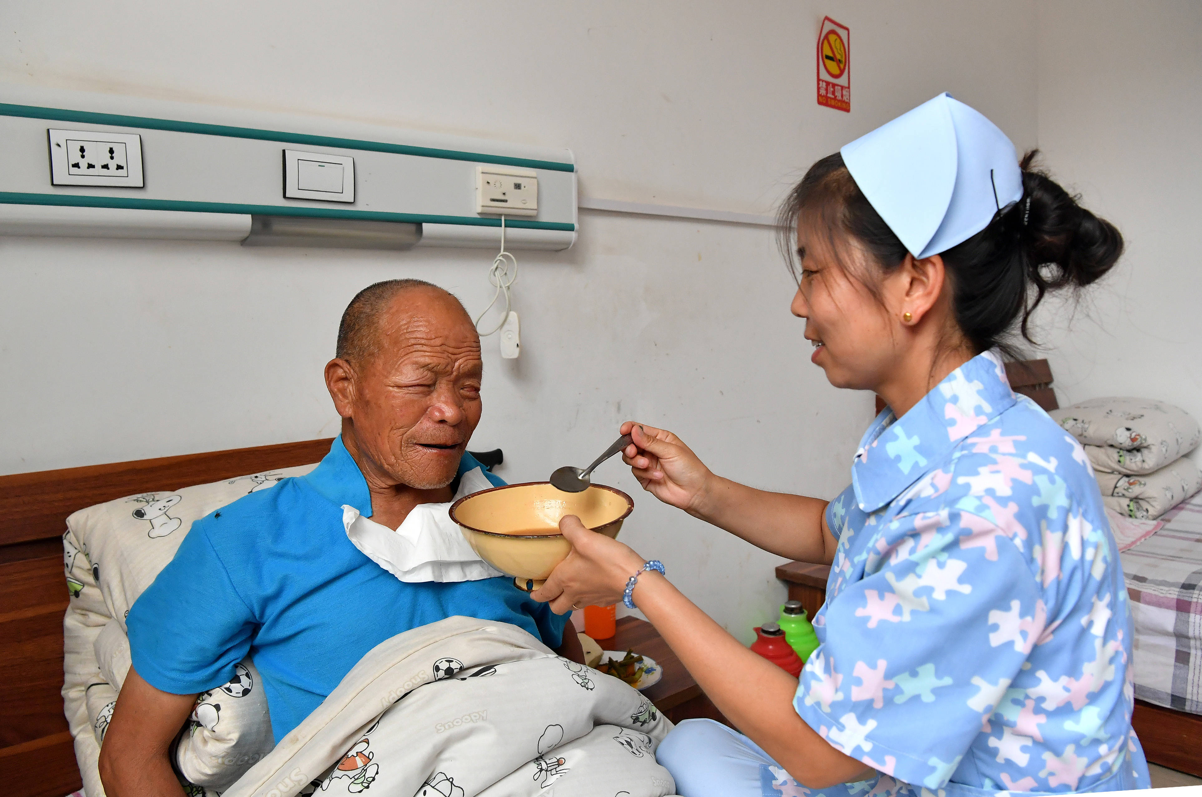 陕西洛南县灵口区域敬老院的工作人员为一位卧床的院民喂饭(7月28日摄