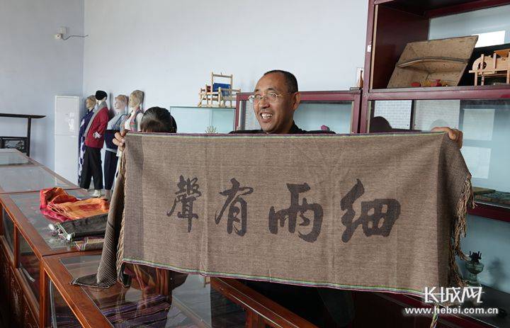 高庆海展示一块老土布艺术品,织有"细雨有声"字样.