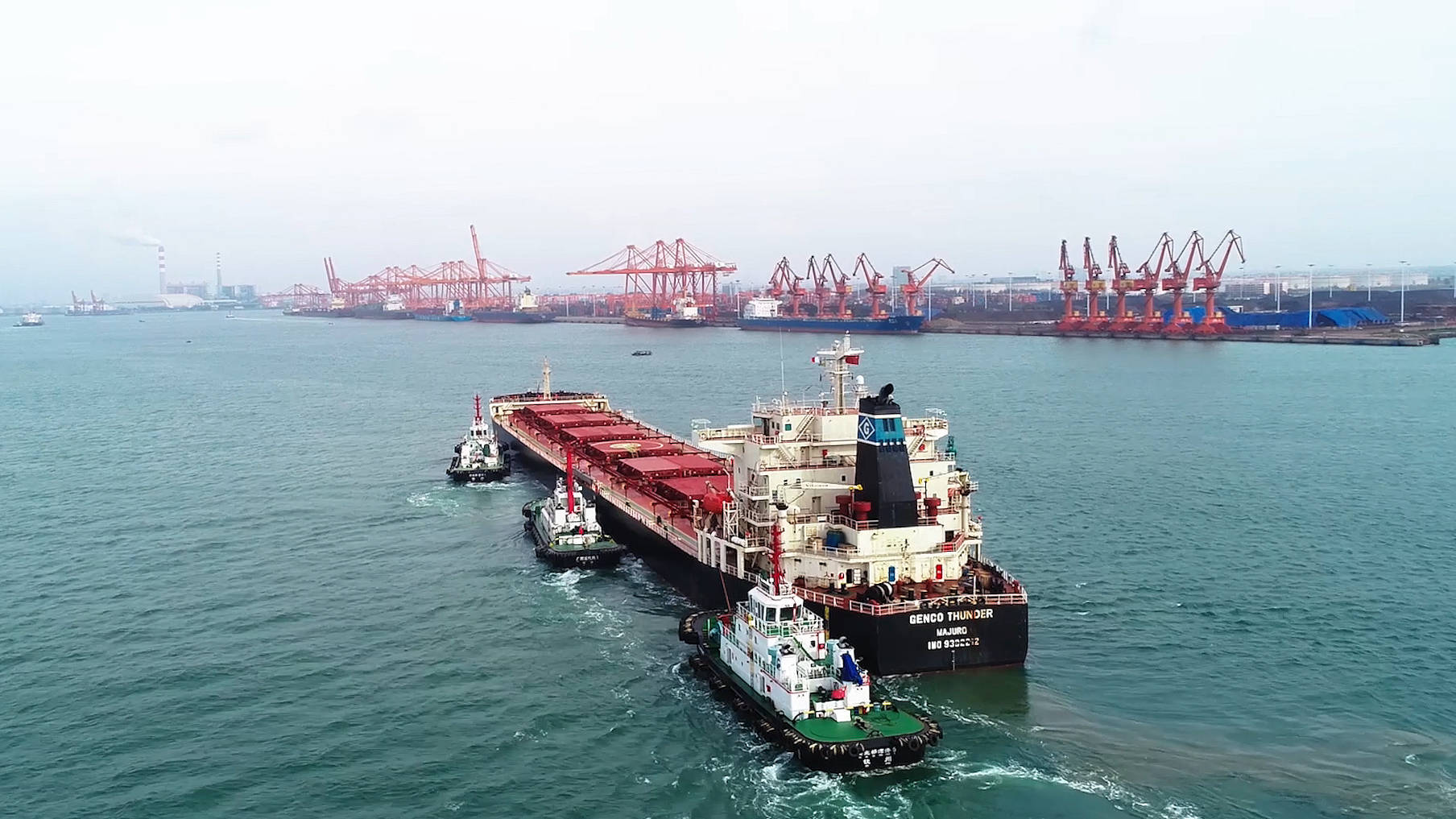 一艘10万吨级海轮在海事船的帮助下停靠广西钦州港码头卸货(无人机