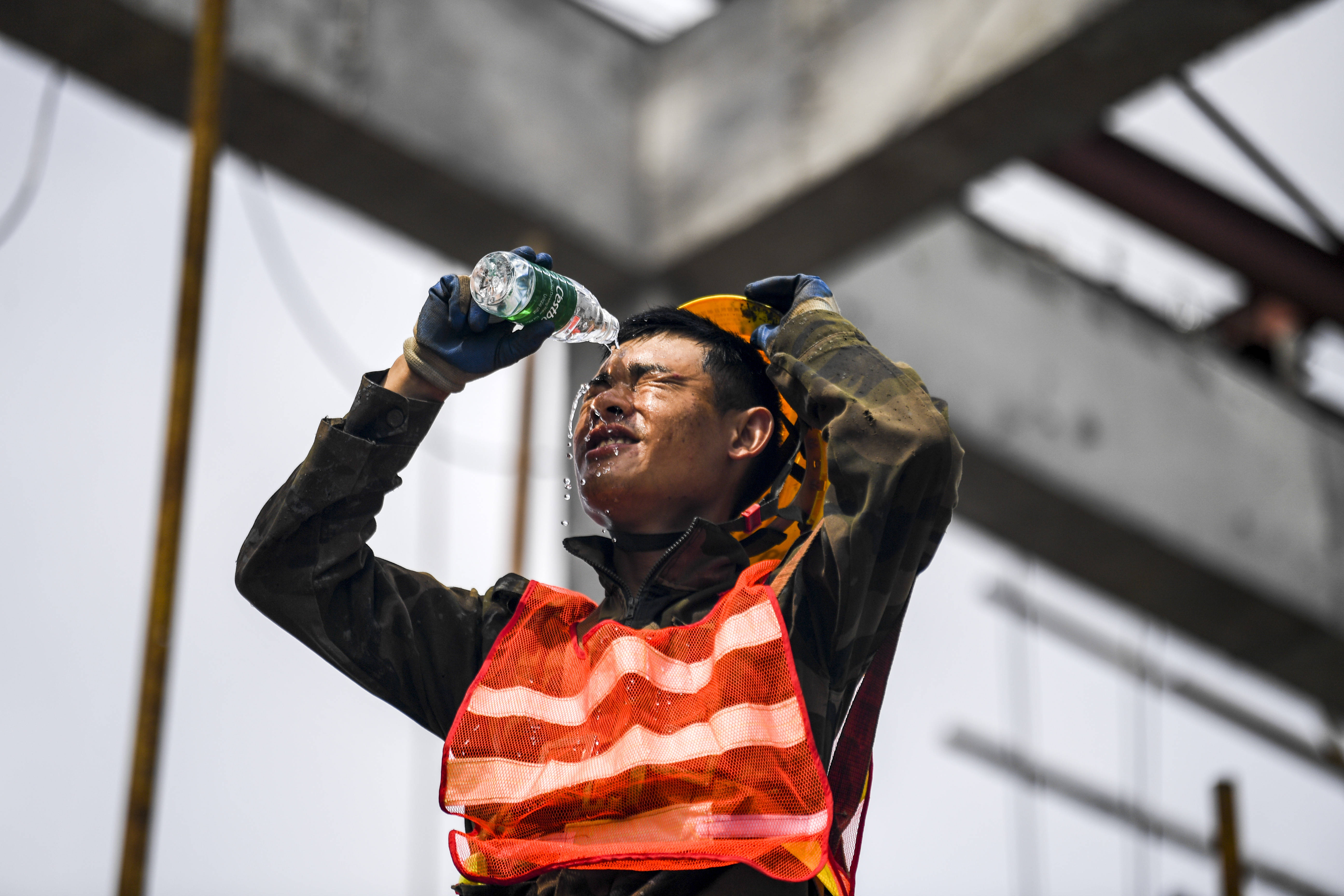 7月9日,在广西南宁市中建三局的一处建设工地上,工人往脸上洒水降温.