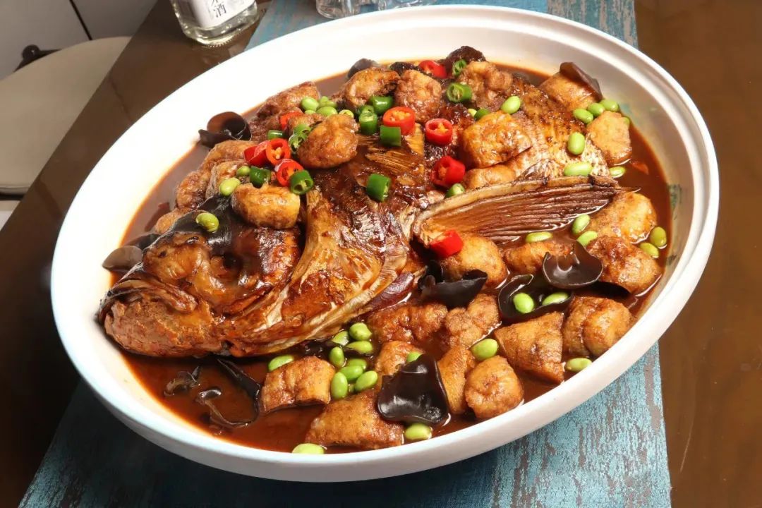 在制作红烧鱼头时,撒入一把剖成两半的油豆腐,使其迅速吸入油汁和鲜味