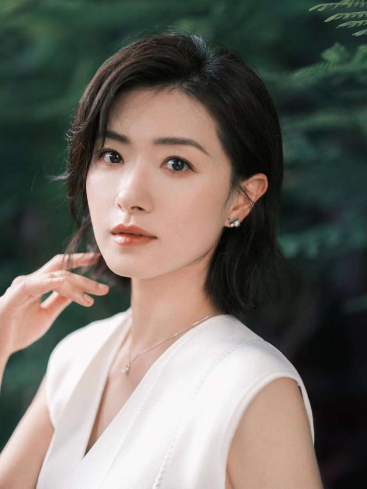 万茜穿白色置身绿衣中,一身无袖连衣裙端庄得体,笑容温婉明媚