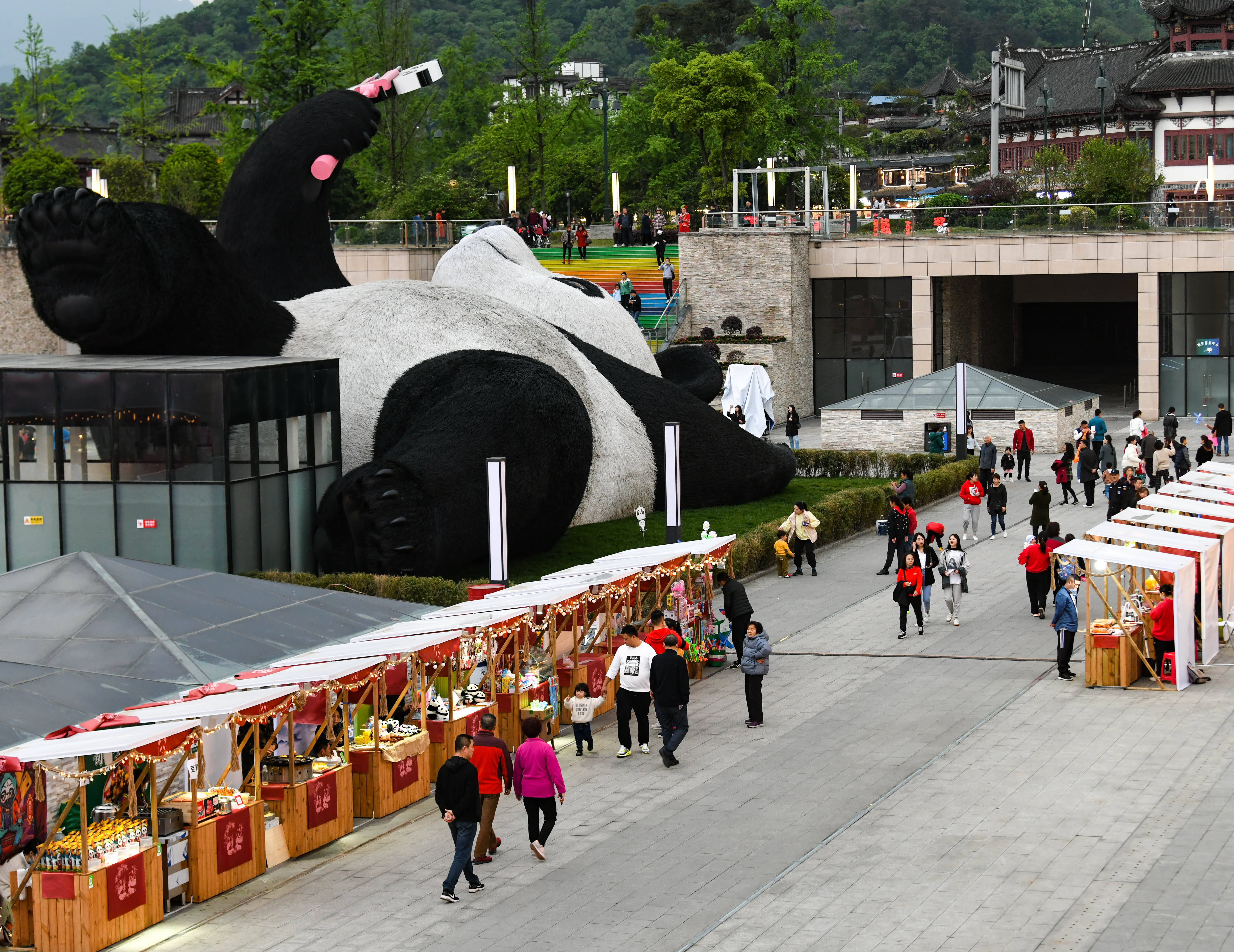 4月7日,在四川省都江堰市仰天窝广场,游客在自拍熊猫雕塑旁边的文创