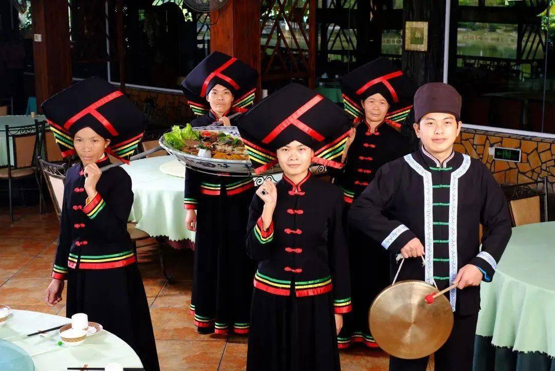 一边引领四位穿着壮族特色服饰的壮家阿姐将壮王土司宴合力"担"上餐桌