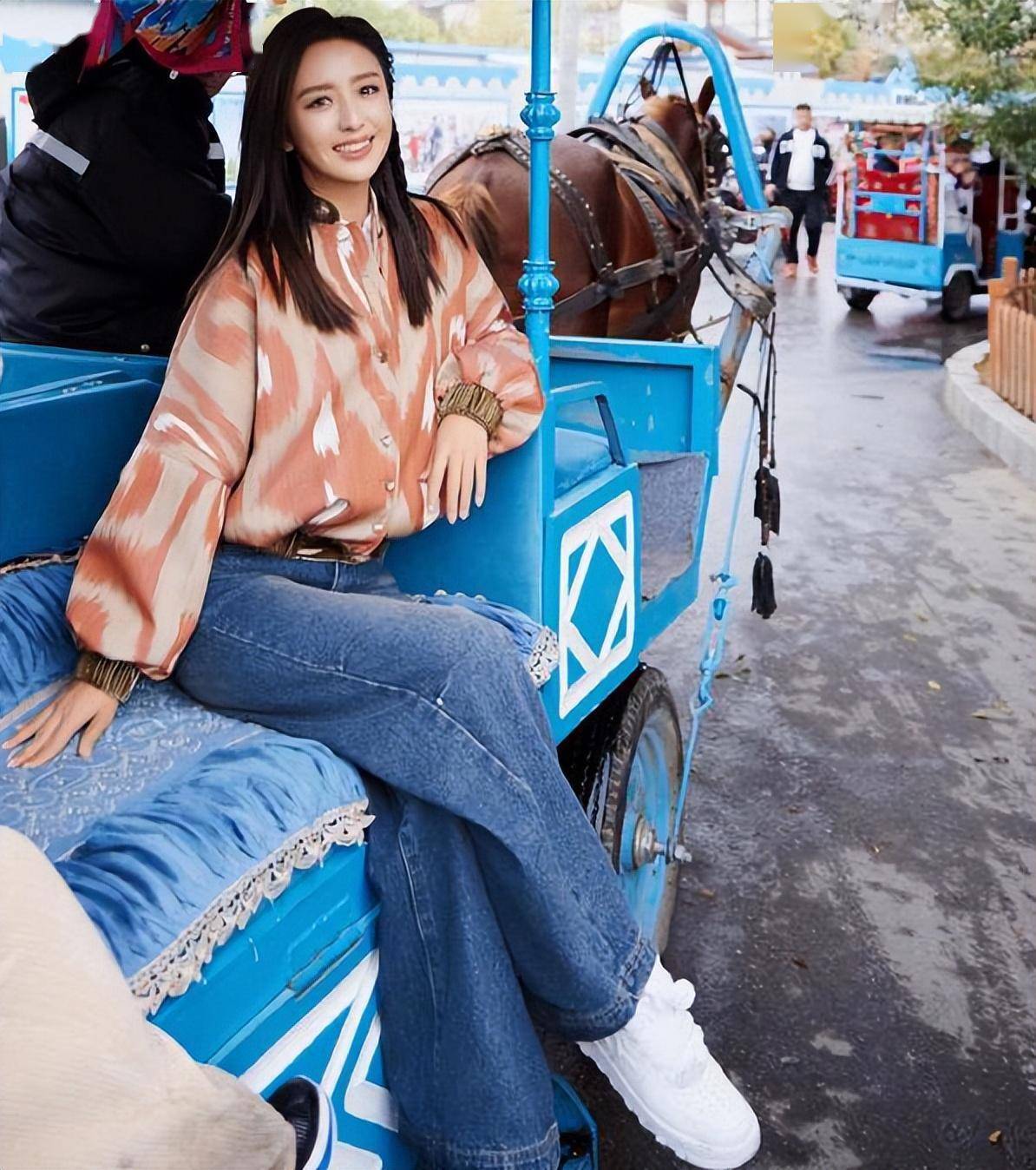 佟丽娅穿着粉色的上衣,搭配蓝色的宽松牛仔裤,脚踩着白色的运动鞋,一